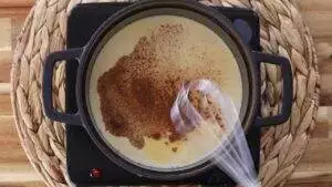 Creamy rice pudding with cinnamon being stirred in a pot on a stove.