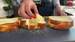 Close-up of a person slicing soft, fresh bread on a cutting board with vibrant red nails.