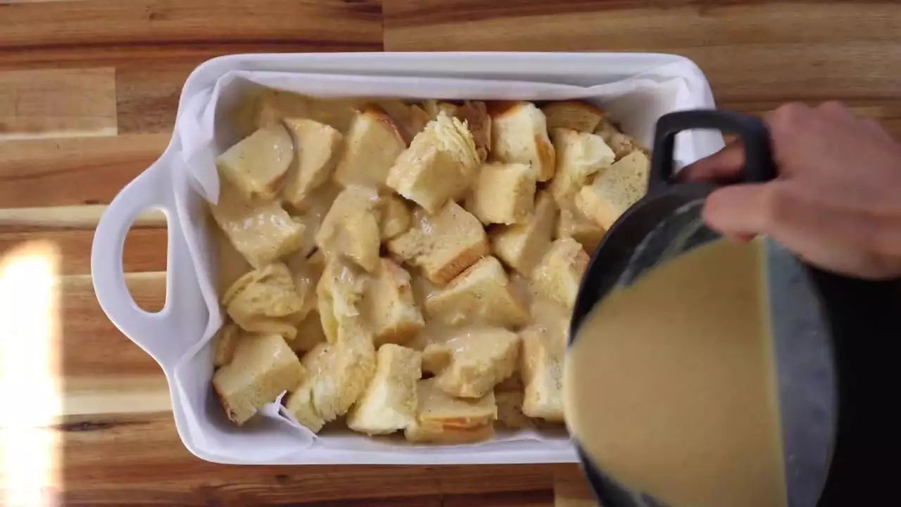 Pouring custard over bread cubes for homemade bread pudding in a white dish, ready for baking.
