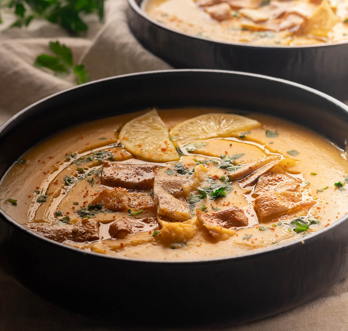 Creamy shorbat adas soup garnished with lemon slices, croutons, herbs, and spices in a black bowl.