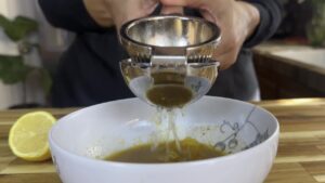 Squeezing fresh lemon juice into a bowl using a metal citrus juicer on a wooden kitchen counter.