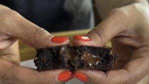 Close-up of hands pulling apart a gooey chocolate cookie with vibrant red nails.