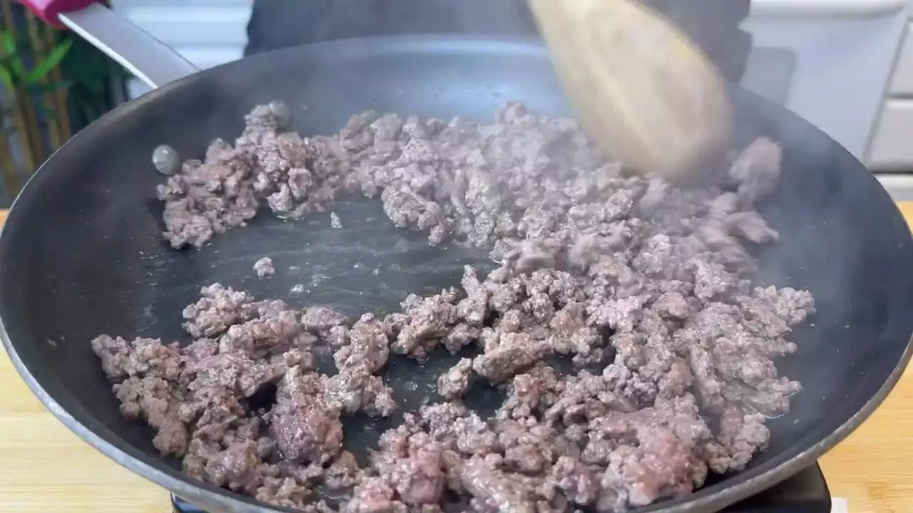 Cooking ground beef in a pan with a wooden spoon, releasing steam. Perfect for tacos or pasta dishes.