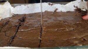 Cutting fresh, homemade brownies on parchment paper in a glass baking dish.