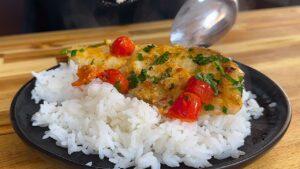 Baked Tilapia Filets with cherry tomatoes and herbs on white rice, served on a black plate.