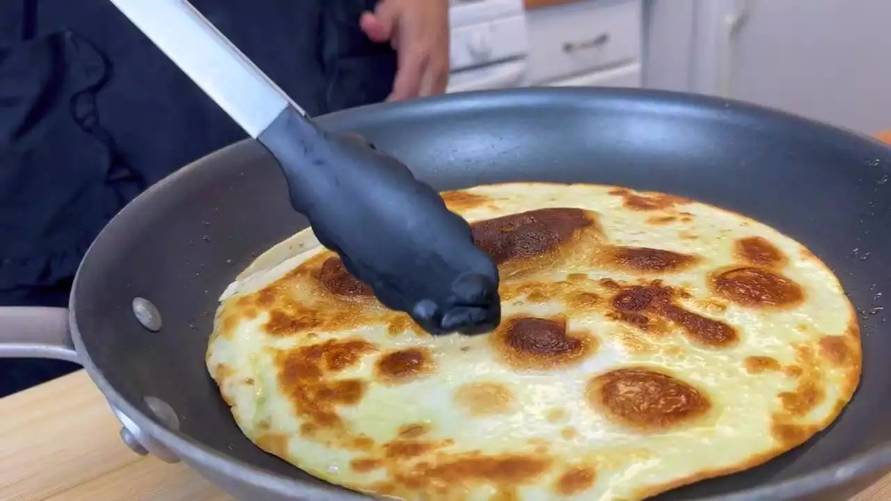 Cooking golden brown quesadilla in pan with tongs in kitchen setting.