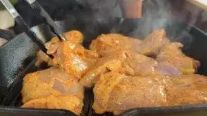 Marinated chicken thighs sizzling on a grill pan with steam rising, held with tongs for a delicious meal.