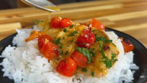 Baked tilapia with cherry tomatoes and herbs on rice, garnished with sauce for a delicious meal.