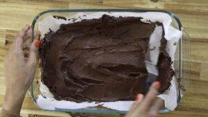 Spreading chocolate batter in a glass dish with a spatula on a wooden table.