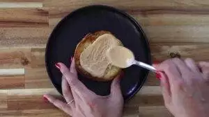 Woman spreading peanut butter on toast with a spoon on a black plate.