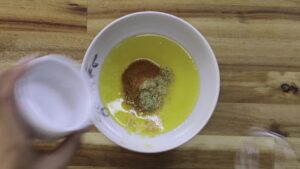 Mixing spices into melted butter in a white bowl on a wooden surface.