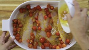 Raw fish fillets with cherry tomatoes drizzled with lemon sauce in a white baking dish.