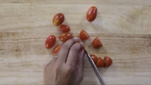 Slicing cherry tomatoes on a wooden cutting board with a knife.