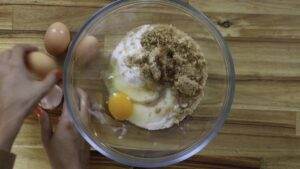 Mixing ingredients for baking: eggs, sugar, and butter in a glass bowl on a wooden surface.