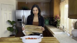 Woman preparing to cover a baking dish with foil in a kitchen.