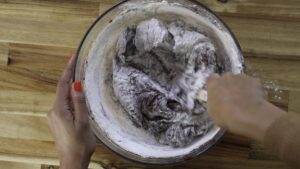 Mixing chocolate cake batter with flour in a glass bowl on a wooden table.