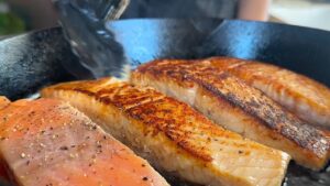 Cooking salmon fillets in a cast iron skillet, highlighting their golden-brown sear and freshness.