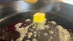 Butter cube melting and sizzling in a hot cast iron pan, creating a rich and flavorful base for cooking.