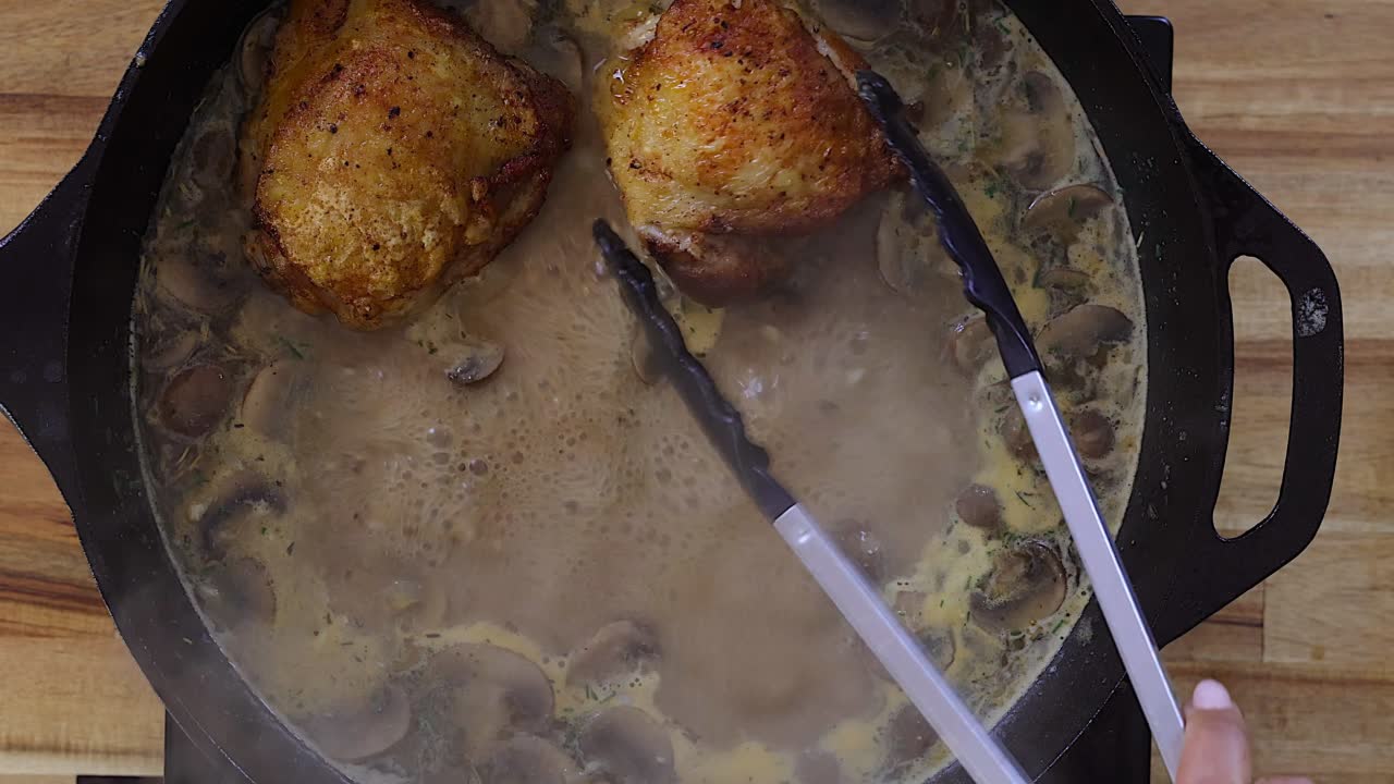 Golden chicken thighs cooking in a creamy mushroom sauce in a cast iron skillet.