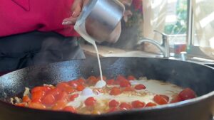 Pouring cream into a skillet with cherry tomatoes for a tasty sauce recipe.