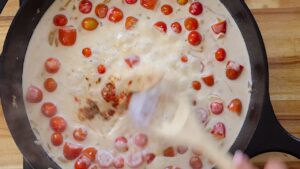 Creamy tomato pasta sauce being stirred in a black skillet on a wooden countertop.