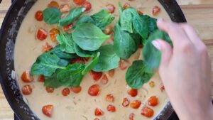 Adding fresh spinach into a steaming sauce.