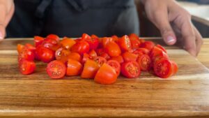 Freshly chopped cherry tomatoes on a wooden cutting board, ready for a salad recipe.