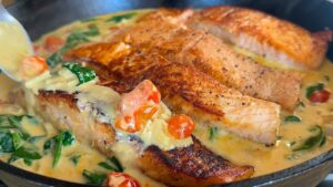 Pan-seared salmon in creamy sauce with tomatoes and spinach, cooked in a skillet.