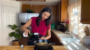 Woman in a kitchen pouring wine into a skillet, preparing a meal at home.