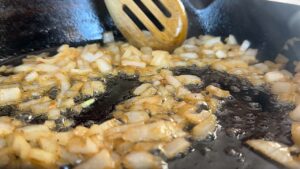 Sautéing onions in a cast iron skillet with a wooden spoon for a savory flavor boost in cooking.