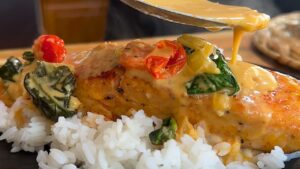 Creamy sauce drizzled on seasoned salmon with tomatoes and spinach, served over a bed of fluffy white rice.