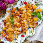 Grilled shrimp skewers with cherry tomatoes and basil on a floral plate.