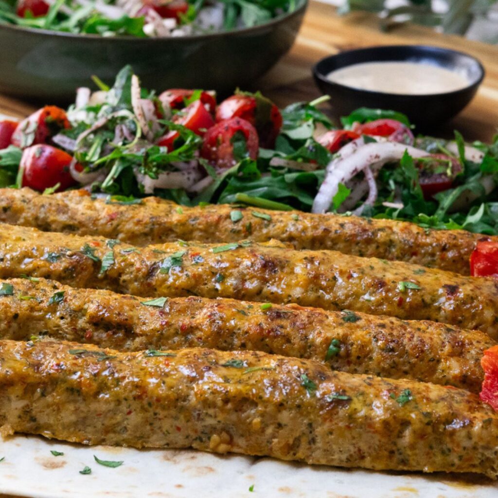 Grilled kebabs with fresh salad and creamy dip on a wooden table.