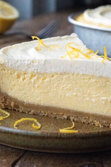 Slice of creamy no bake lemon mascarpone cheesecake with zest garnish on a ceramic plate, half lemon and fork in background.