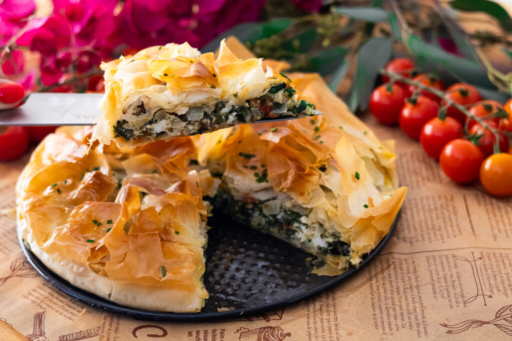 Freshly baked Mediterranean Spinach Pie with Puff Pasty with golden phyllo crust, served on a plate, cherry tomatoes in background.
