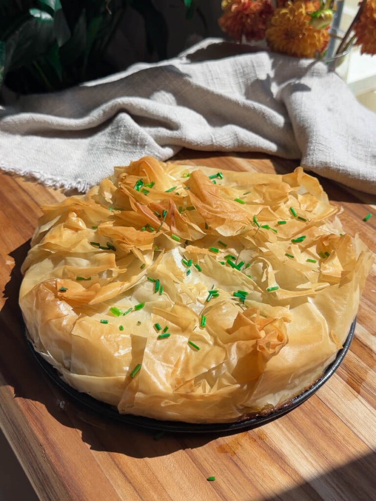Mediterranean phyllo pie topped with fresh chives on a wooden table.