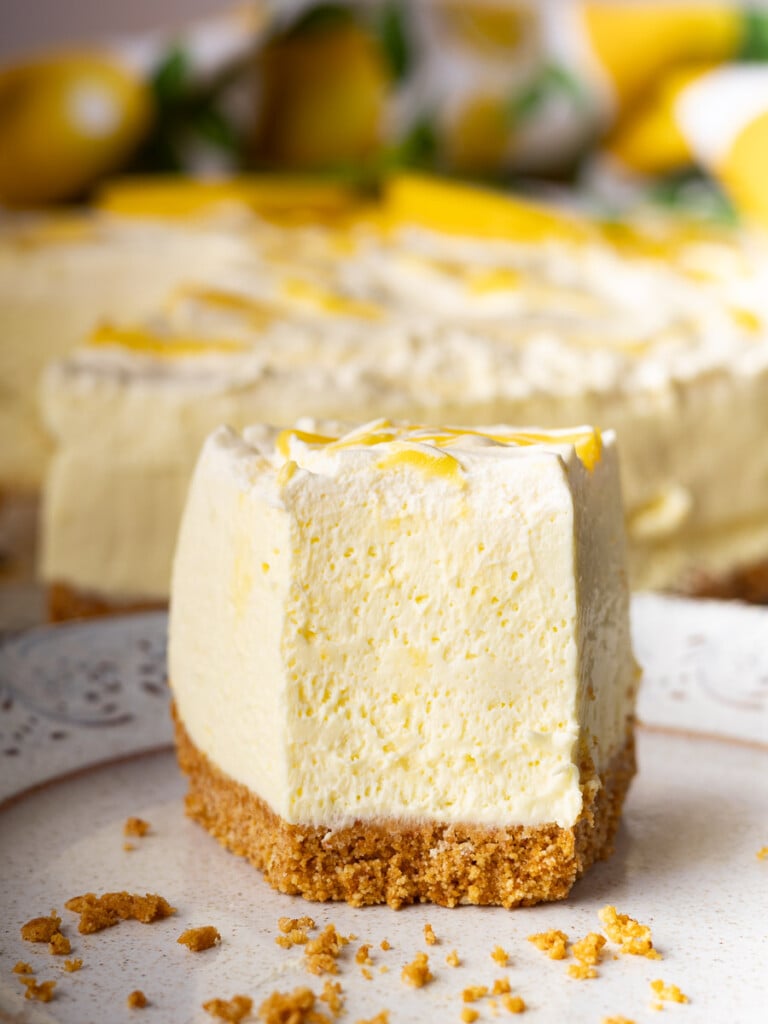Slice of no-bake lemon mascarpone cheesecake  on a plate with a graham cracker crust, topped with lemon zest.