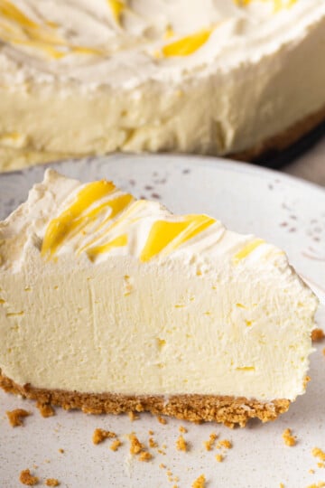Slice of no-bake lemon mascarpone cheesecake with a swirl topping on a decorative plate, with graham cracker crust.