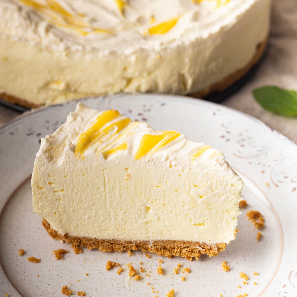 Slice of no-bake lemon mascarpone cheesecake with a swirl topping on a decorative plate, with graham cracker crust.