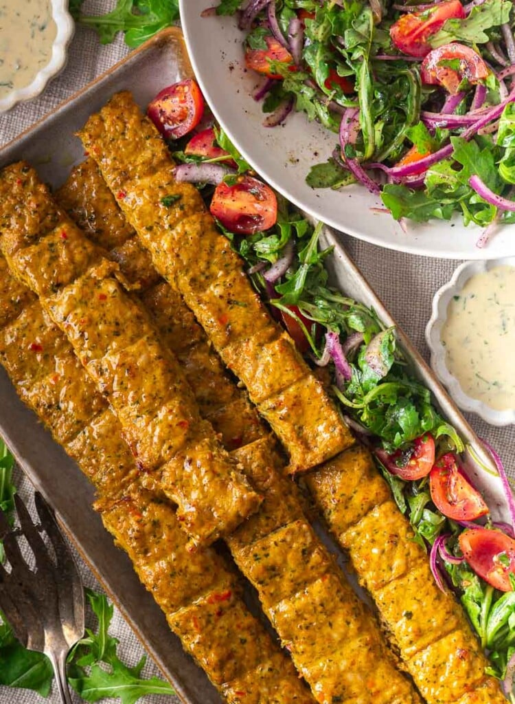 Sheet pan chicken kebabs in the oven with a side salad of cherry tomatoes, arugula, and onions, served with a creamy dressing.