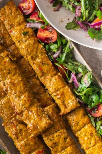 Sheet pan chicken kebabs in the oven with salad and dipping sauce on a platter, featuring tomatoes and arugula.