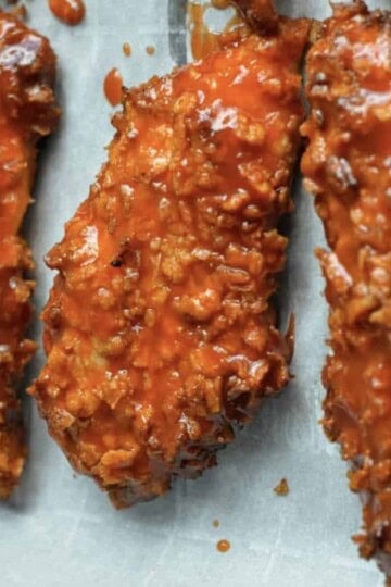 Crispy baked chicken tenders coated in spicy buffalo sauce on parchment paper, a savory and flavorful dish.