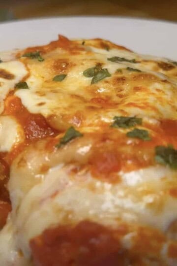 Delicious homemade chicken parm with melted cheese and fresh herbs on a white plate.