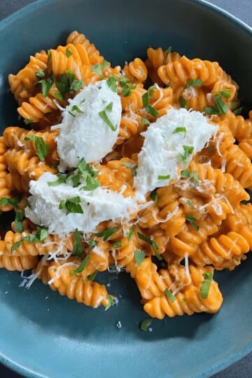 Creamy pasta topped with cheese and herbs in a blue bowl, showcasing a delicious, savory dish.