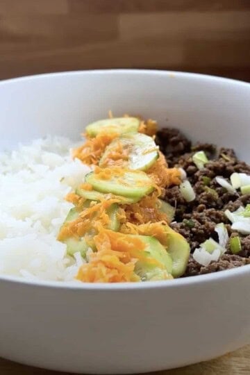 Rice bowl with ground beef, shredded carrots, and green onions in a white bowl. Perfect healthy meal option.