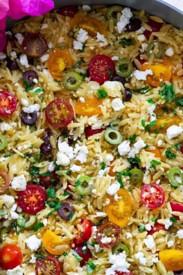 Colorful Mediterranean orzo salad with cherry tomatoes, olives, feta cheese, and parsley in a bowl.