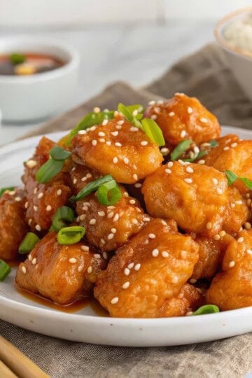 healthy orange chicken topped with sesame seeds and green onions, served with rice and sauce.