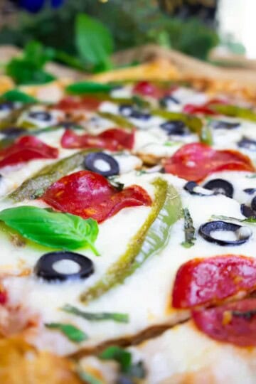 Close-up of a freshly baked pizza topped with pepperoni, olives, and green peppers, garnished with basil leaves.