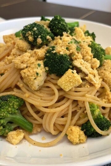 Plate of spaghetti with broccoli and crumbled tofu, served on a white plate, perfect for a vegan meal idea.
