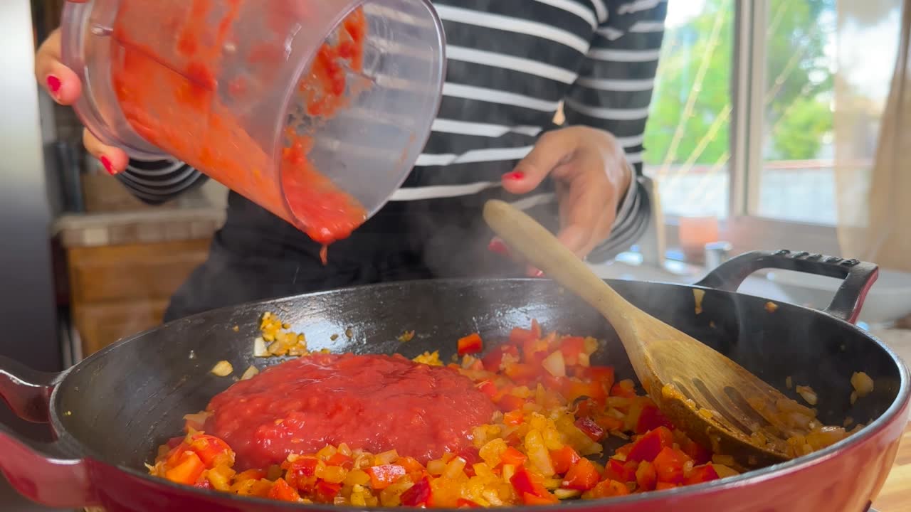 Person adding tomato sauce to skillet.